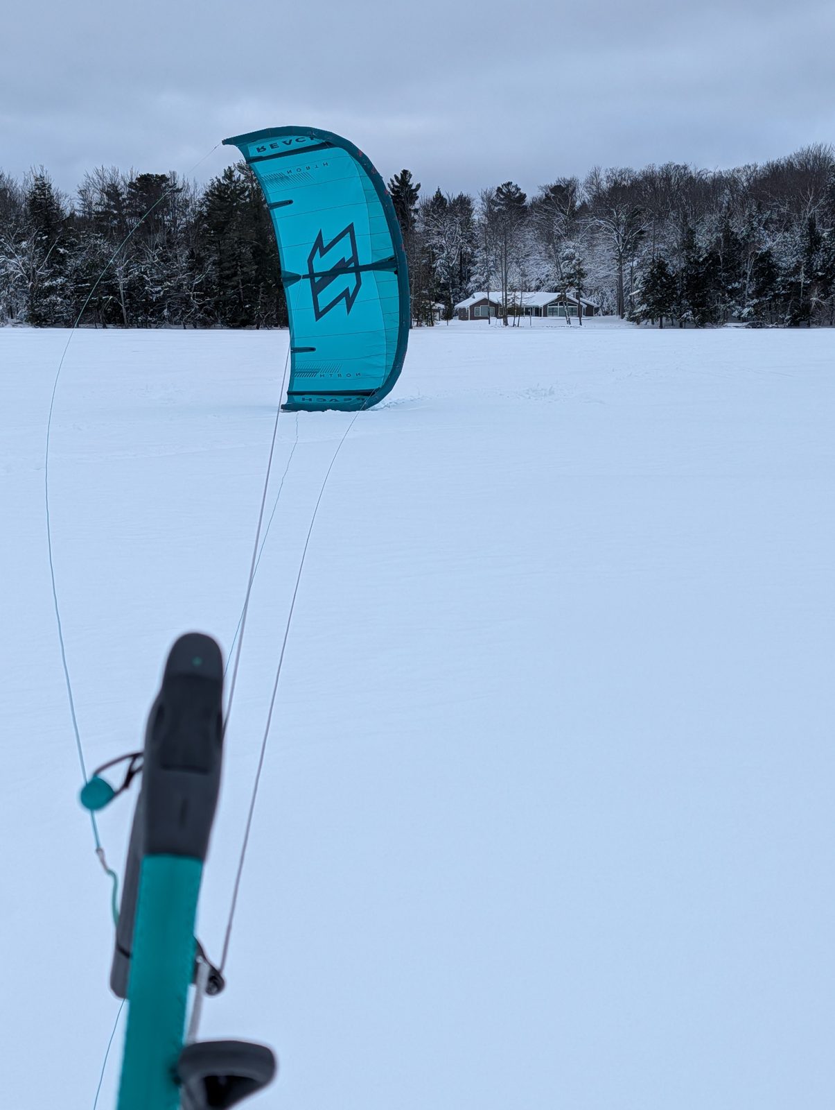 A teal kite flying over a snowy frozen lake