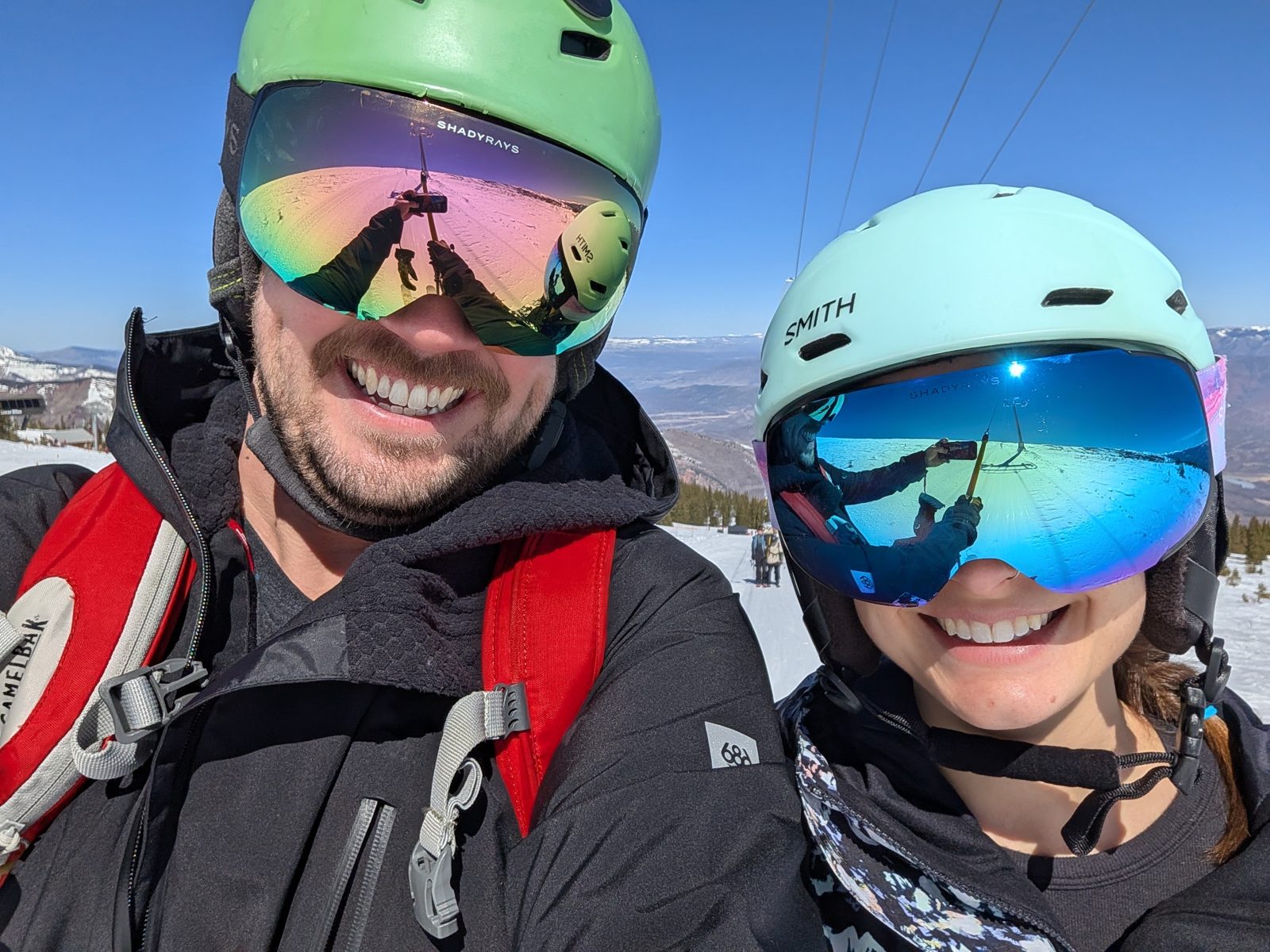 Two people in ski helmets and goggles smiling for a selfie on the mountain