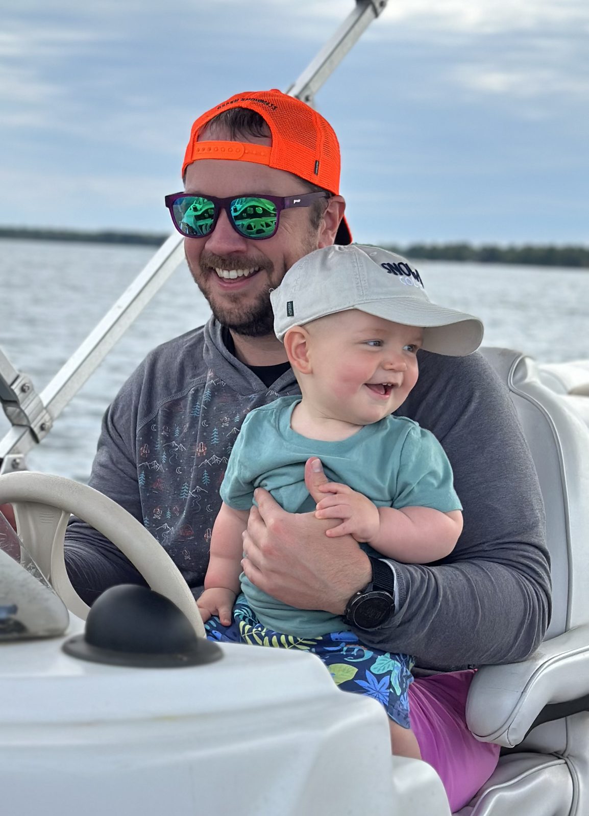 A man in an orange cap and sunglasses holding a smiling baby on a boat