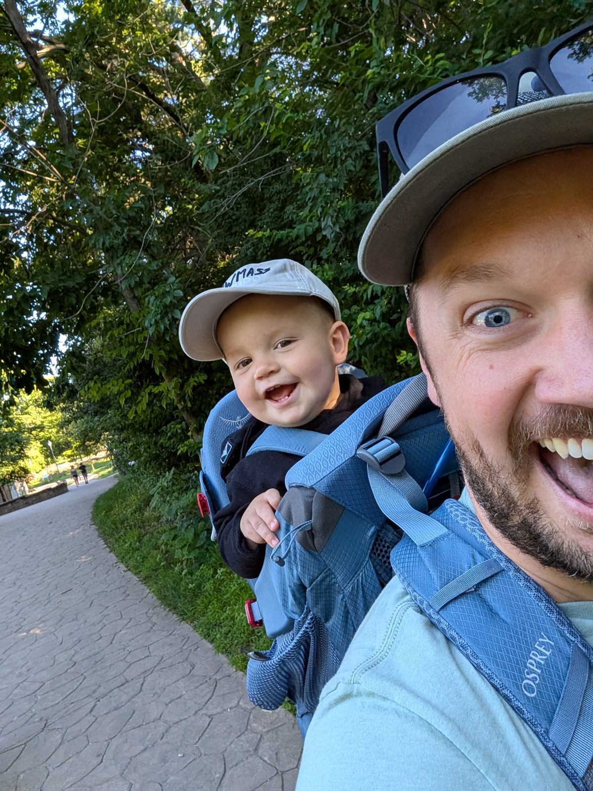 A man taking a selfie on a path with a baby riding in a hiking backpack behind him