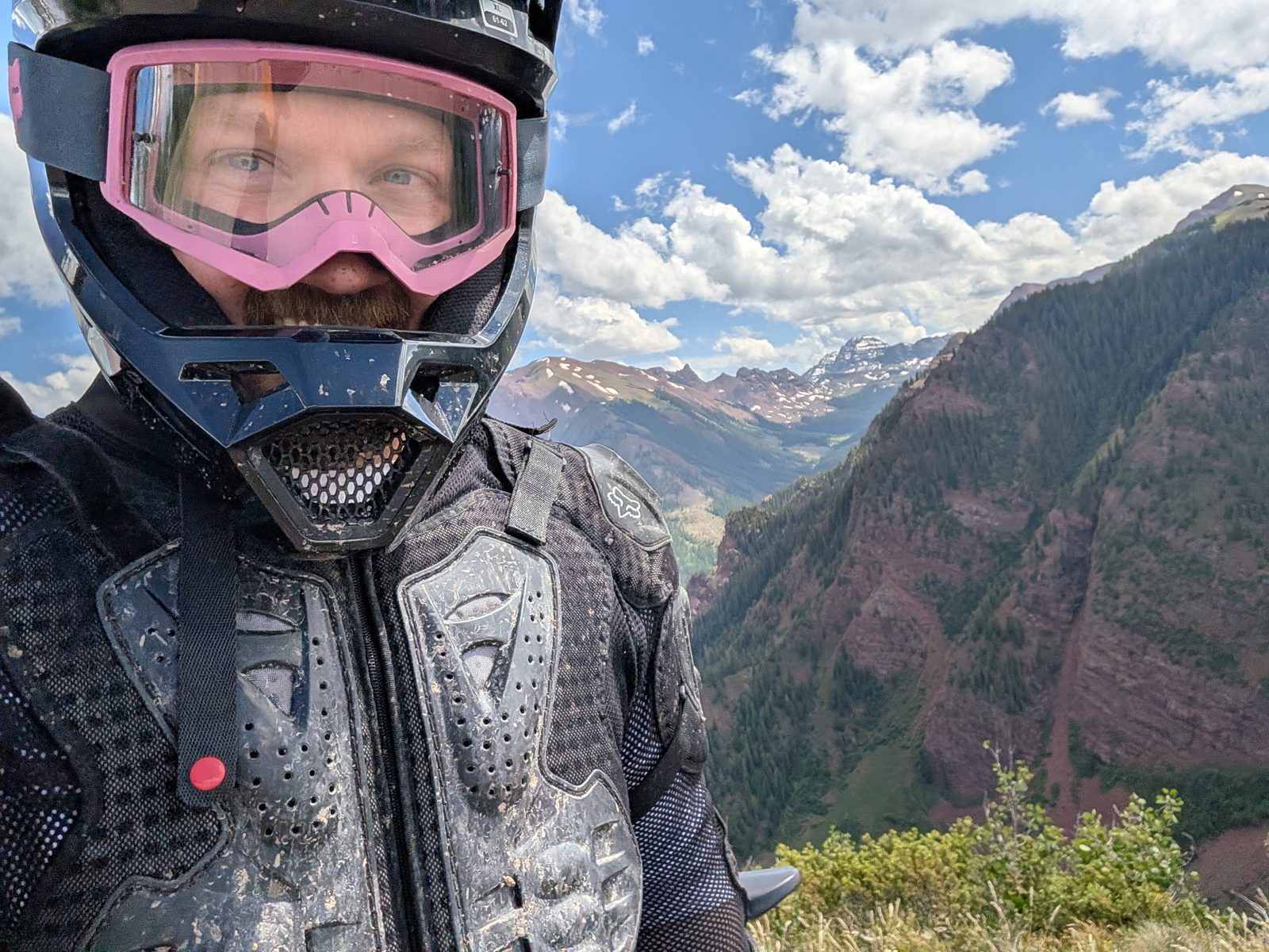 A rider in a helmet and pink goggles with a mountain valley behind