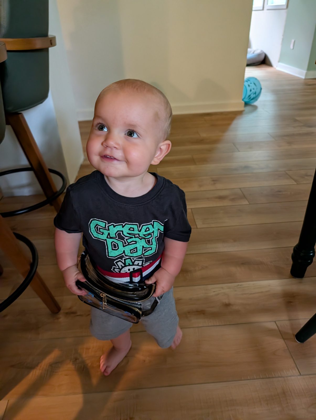 A toddler in a Green Day t-shirt smiling at the camera on a wood floor
