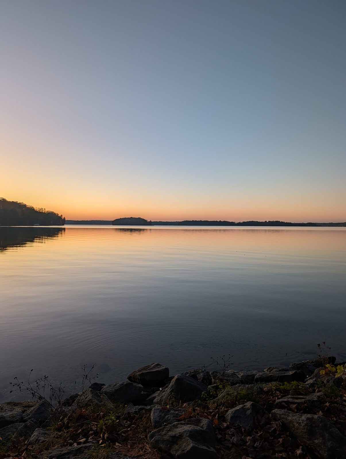 Sunset over a calm lake with a rocky shoreline