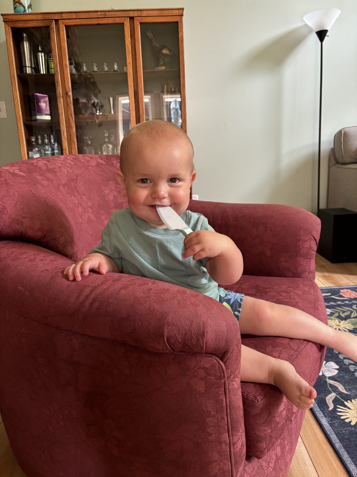 A baby in a red armchair chewing on a white utensil